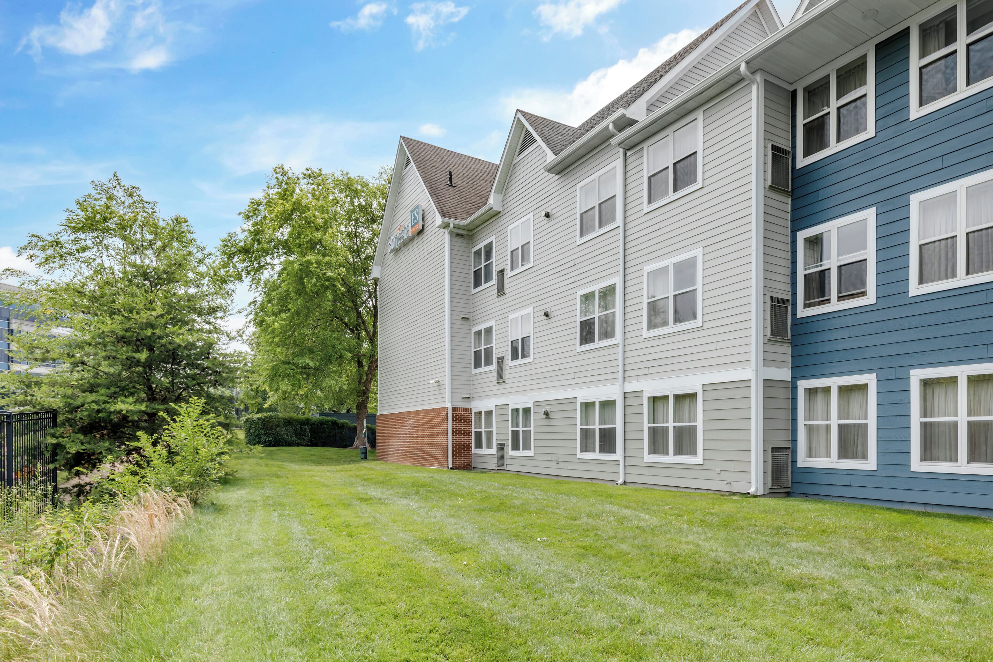 A multi-story residential building with a well-maintained lawn and a brick foundation.