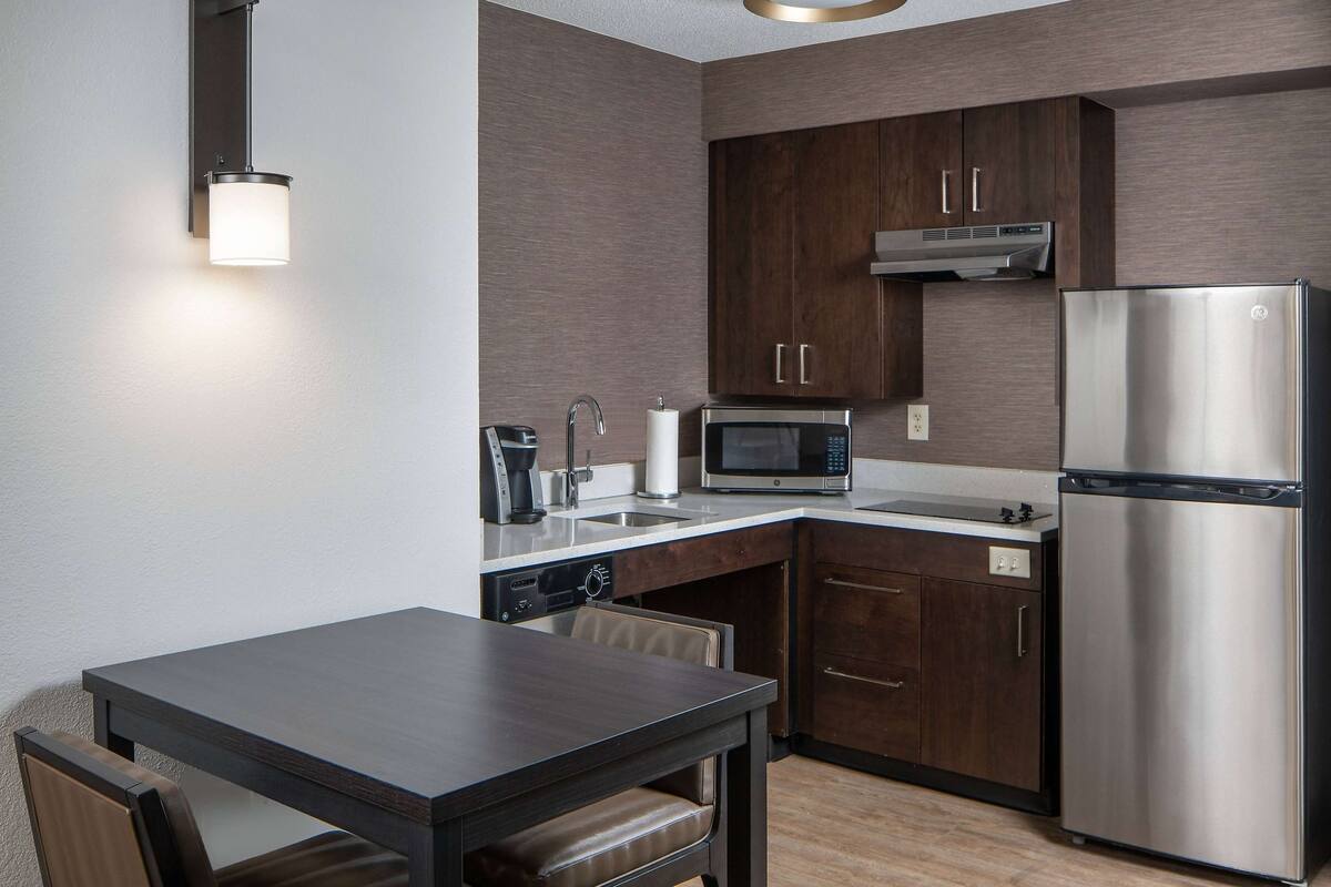 Una cocina moderna con armarios de madera oscura, electrodomésticos de acero inoxidable, microondas integrado y un comedor con mesa y sillas.
