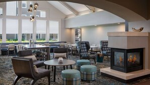 A spacious lounge area with a fireplace, comfortable seating, and large windows offering a view of the outdoors. - Sonesta ES Suites Fairfax Fair Lakes (Fairfax)