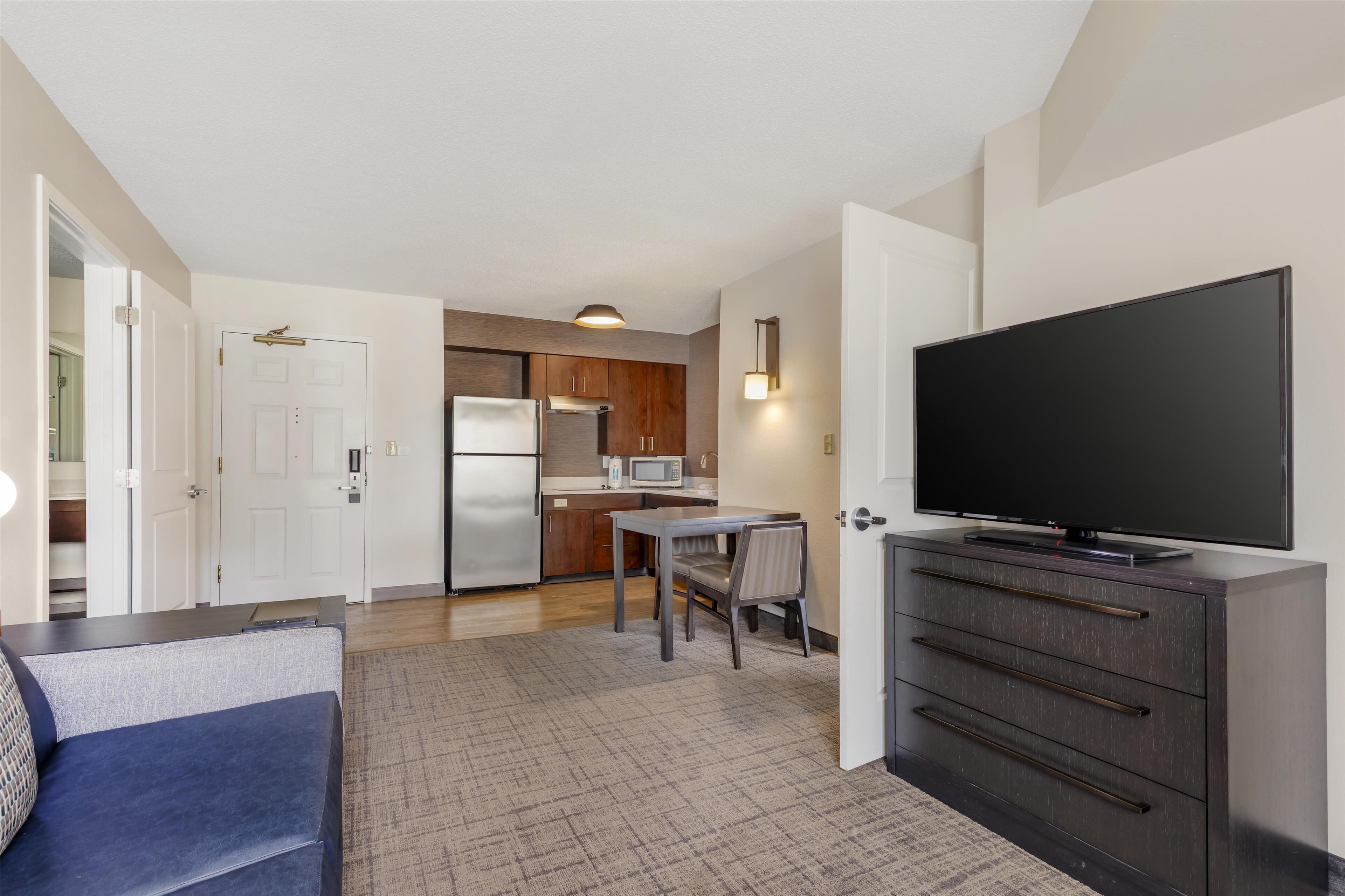 Un espacio habitable pequeño con kitchenette, comedor y televisor sobre un aparador.