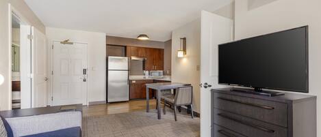Un espacio habitable pequeño con kitchenette, comedor y televisor sobre un aparador.