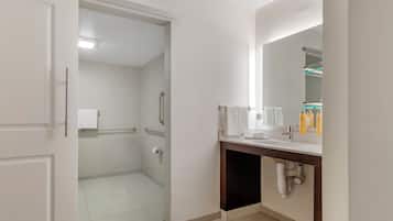 Un baño moderno con inodoro, lavabo y espejo. Se ve un perchero y una zona de ducha al fondo.