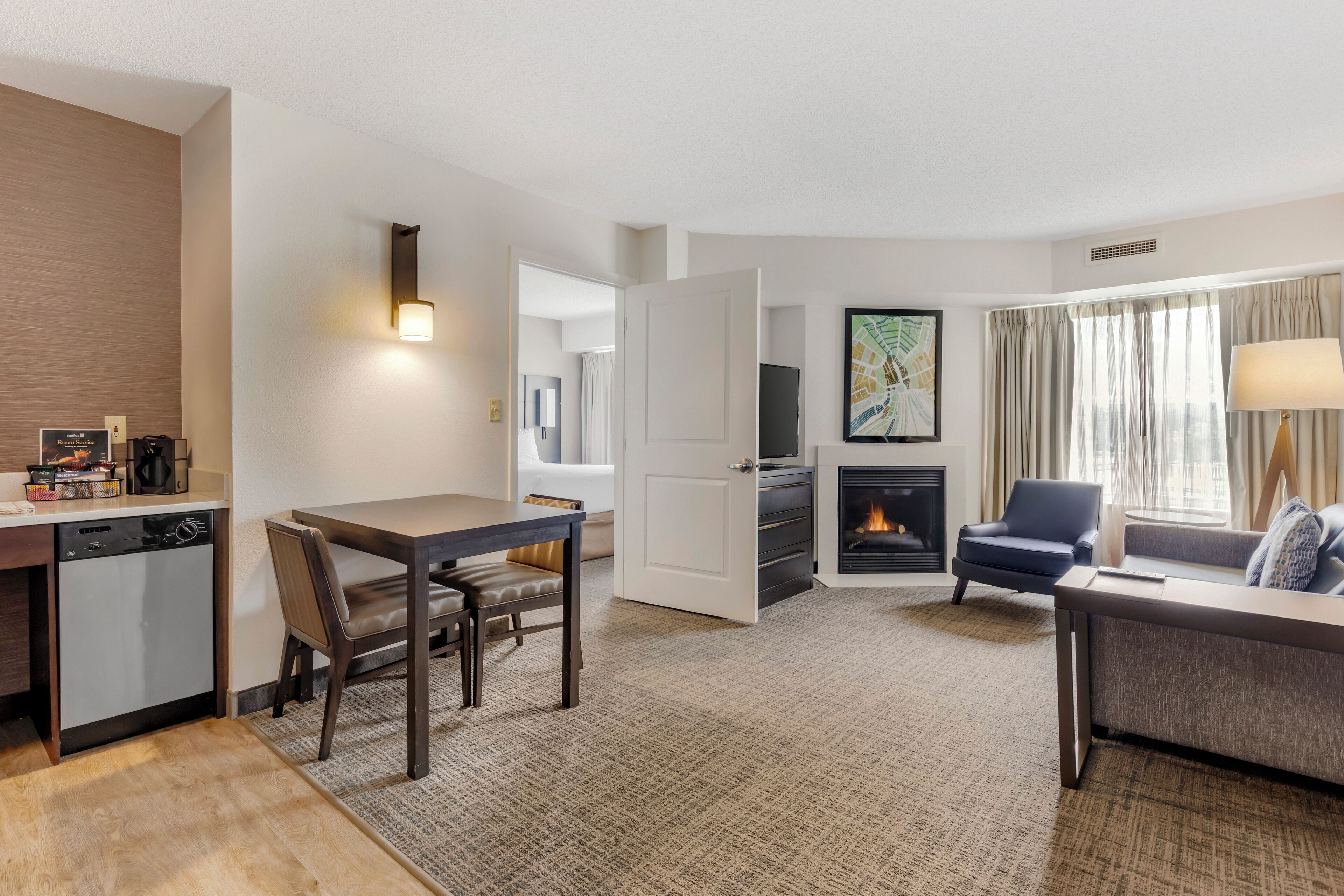 A modern hotel room with a dining area, a living room with a fireplace, and a sofa.
