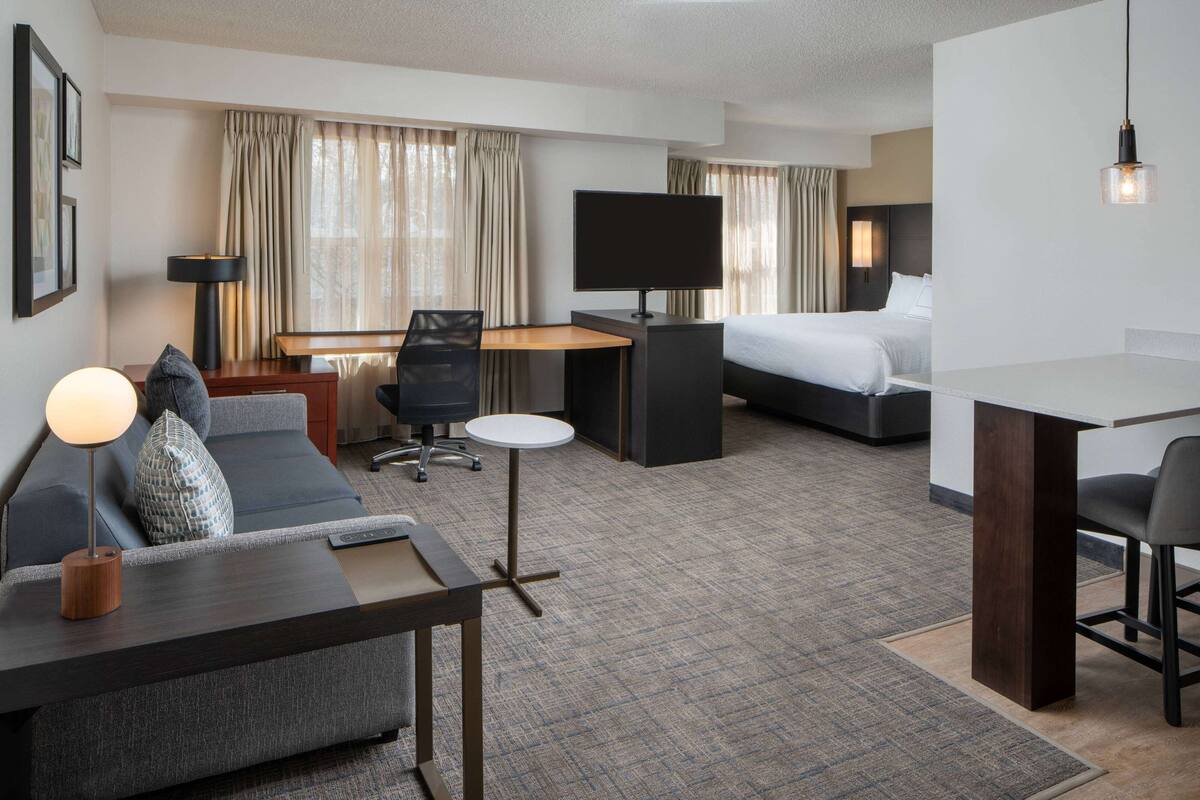 Una habitación de hotel con cama, escritorio con computadora, sofá, sillón y televisión.