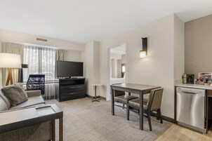 Habitación de hotel moderna con sofá, televisión, mesa de comedor y zona de cocina.