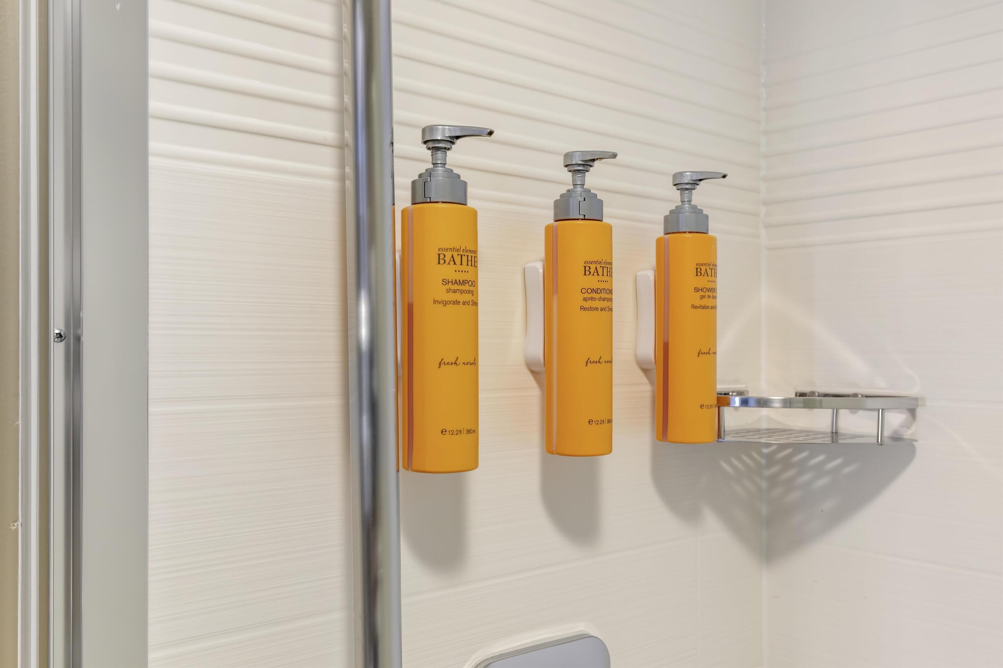 A bathroom with three yellow bottles of BATH & BODY SHOP shampoo and conditioner on a wall-mounted rack.