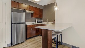 A modern kitchen with stainless steel appliances, wooden cabinets, and a bar area with stools. - Sonesta ES Suites Fairfax Fair Lakes (Fairfax)