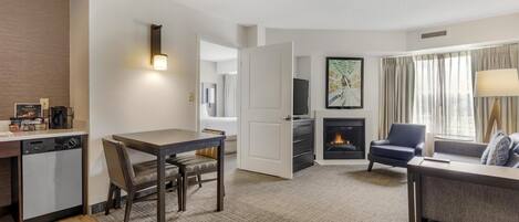 A modern hotel room with a dining area, a sofa, a fireplace, and a television.