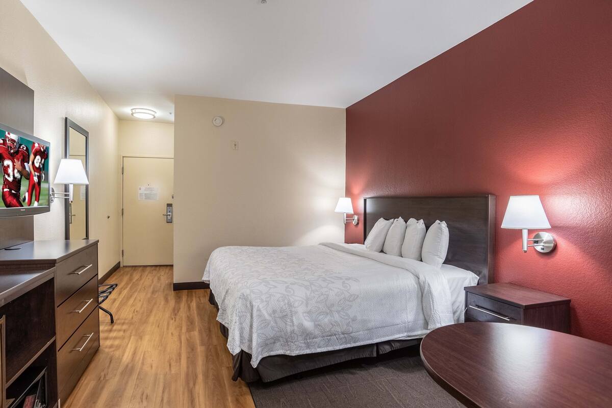A hotel room with a bed, bedside tables, a TV, and a desk.