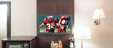 Habitación de hotel con una televisión mostrando un partido deportivo, un escritorio con una lámpara y una silla.