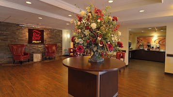 Un hall d’hôtel avec un comptoir d’accueil, un grand arrangement floral et un panneau indiquant « Red Roof Plus+ ».
