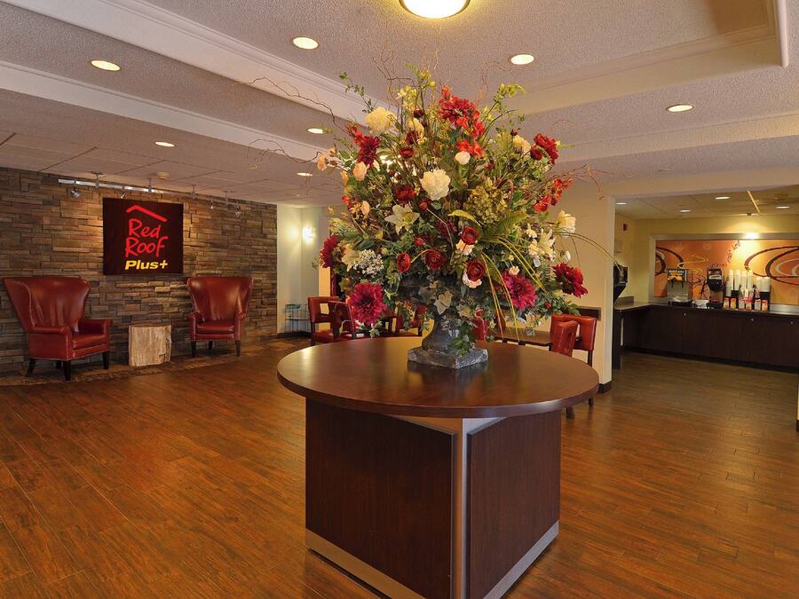 Un hall de hotel con mostrador de recepción, un gran centro de flores y un letrero que dice 'Red Roof Plus+'.
