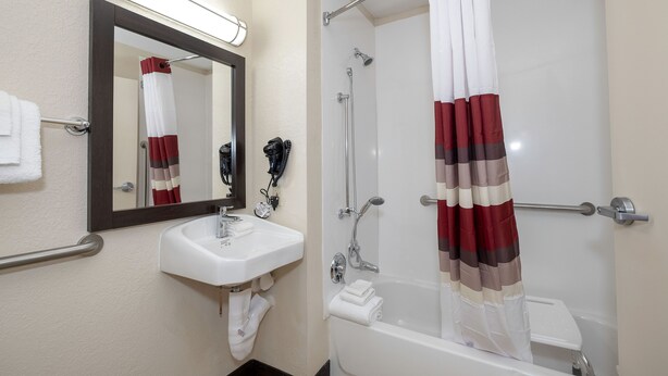 A bathroom with a white sink, a mirror, a shower with a red and white striped curtain, and a towel rack.