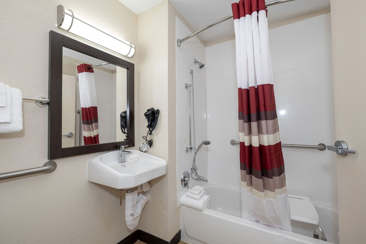 Un baño con un lavamanos blanco, un espejo, una ducha con cortina a rayas rojas y blancas, y un perchero para toallas.