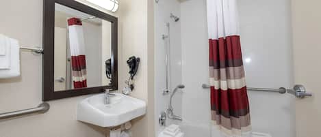 Un baño con un lavamanos blanco, un espejo, una ducha con cortina a rayas rojas y blancas, y un perchero para toallas.