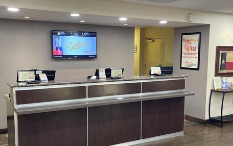 A reception desk with a digital screen displaying a welcome message, a parking sign, and a framed flag.