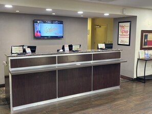 A reception desk with a digital screen displaying a welcome message, a parking sign, and a framed flag. - Red Roof Inn PLUS+ San Antonio Downtown - Riverwalk (San Antonio)