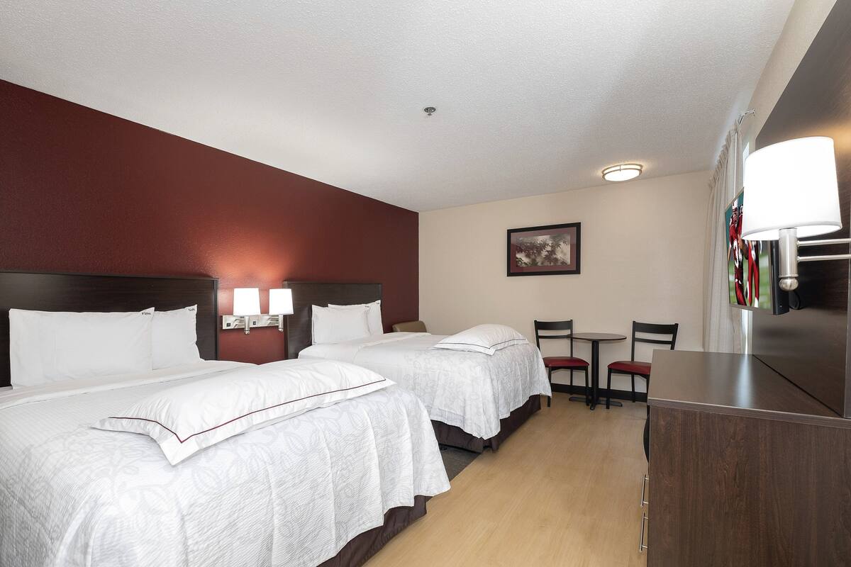 A hotel room with two beds, a desk, a chair, a table, and a lamp.