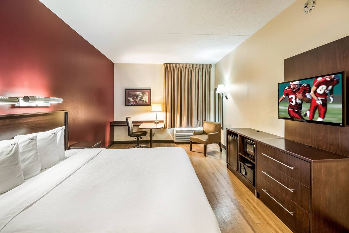 A hotel room with a large bed, a desk with a chair, a television, and a wardrobe.