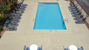A rectangular pool with a clear blue surface, surrounded by lounge chairs and tables.