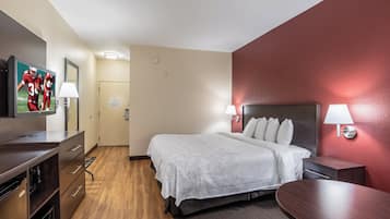 A hotel room with a bed, bedside lamps, a desk, a television, and a wooden floor.