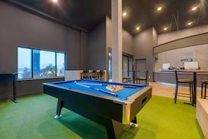 A pool table in a hotel room with a view of the city through a large window. - Clarion Pointe Wesley Chapel - Tampa Area (Wesley Chapel)