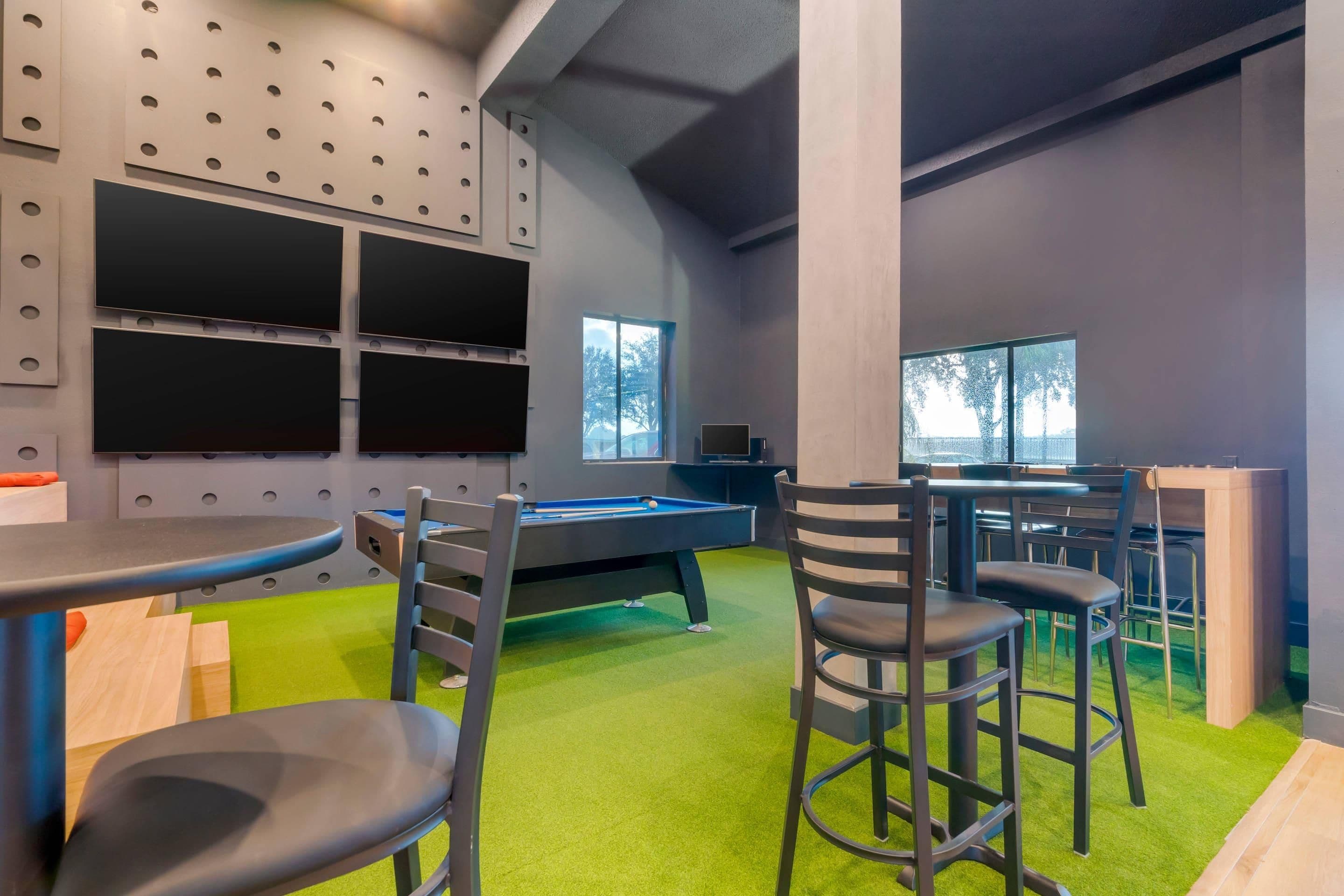 Una habitación con mesa de billar, sillas, una zona de bar y una pared con varias pantallas.