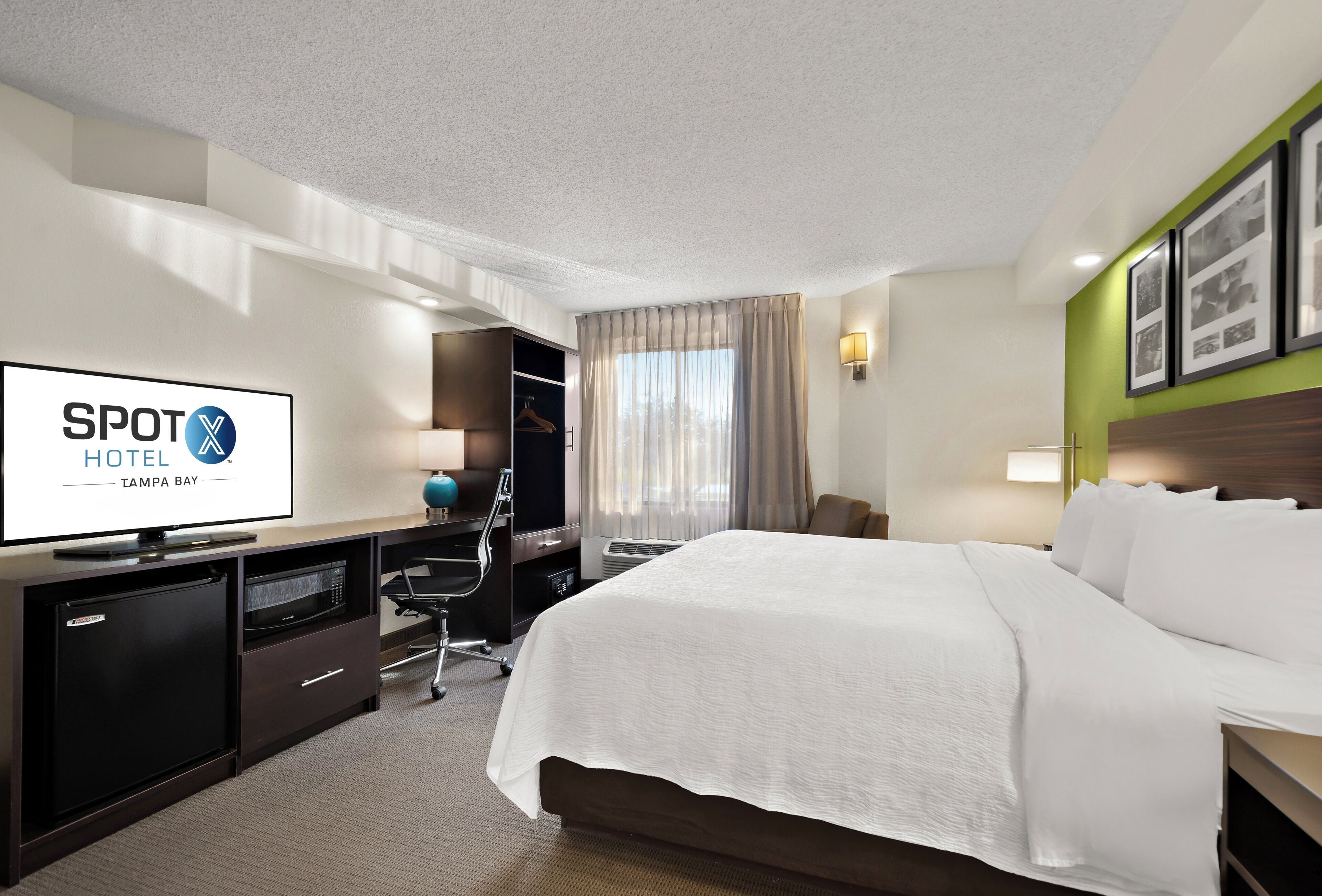 A hotel room with a bed, a desk with a computer, a TV, and a minibar.