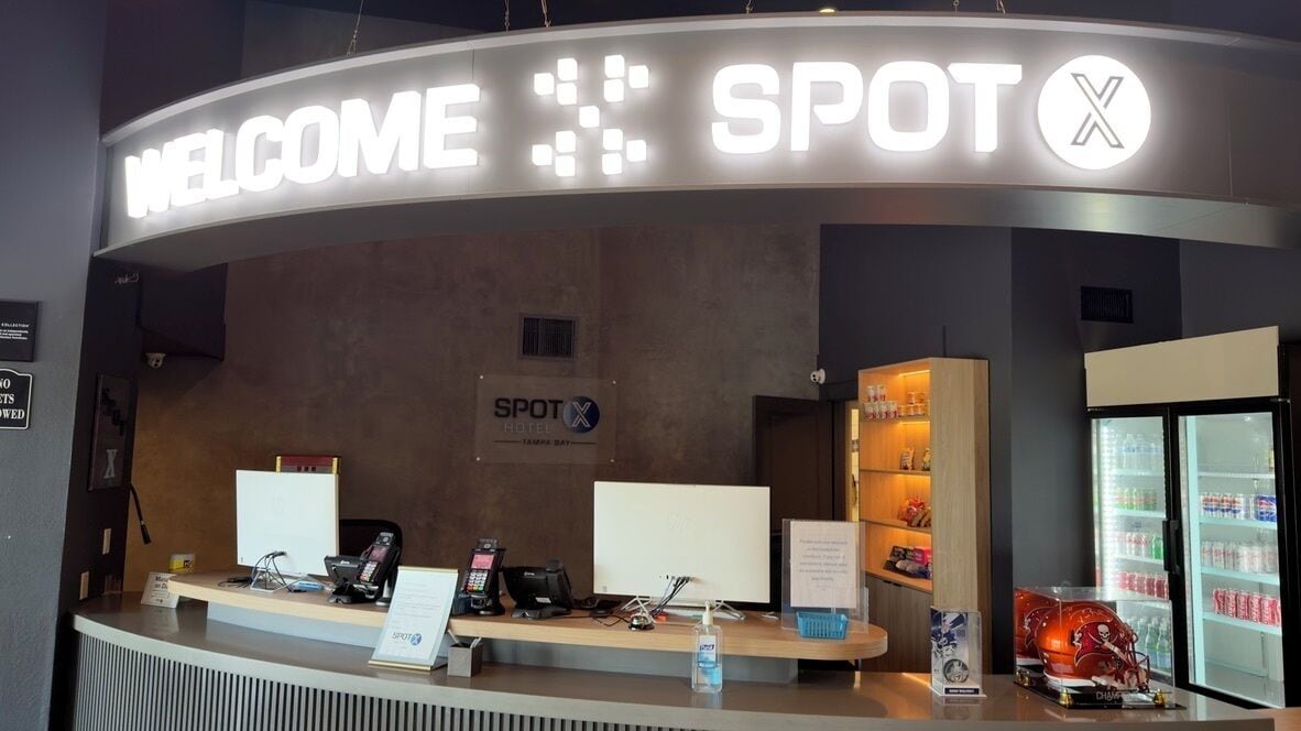 Un comptoir d’accueil avec une pancarte « BIENVENUE », le logo « SPOT », un tableau blanc, un téléphone, un ordinateur et un réfrigérateur contenant des bouteilles d’eau.