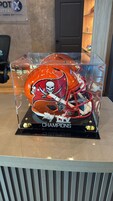 Vitrina de exhibición de trofeos con un casco de fútbol y la palabra 'CHAMPIONS' sobre un pedestal negro.