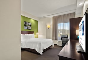 A hotel room with a bed, a desk, a chair, a lamp, and a window with curtains.