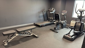 Een sportschool met loopbanden, een hometrainer en een bank.