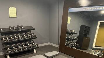 A gym with a bench press, dumbbells, and a mirror.