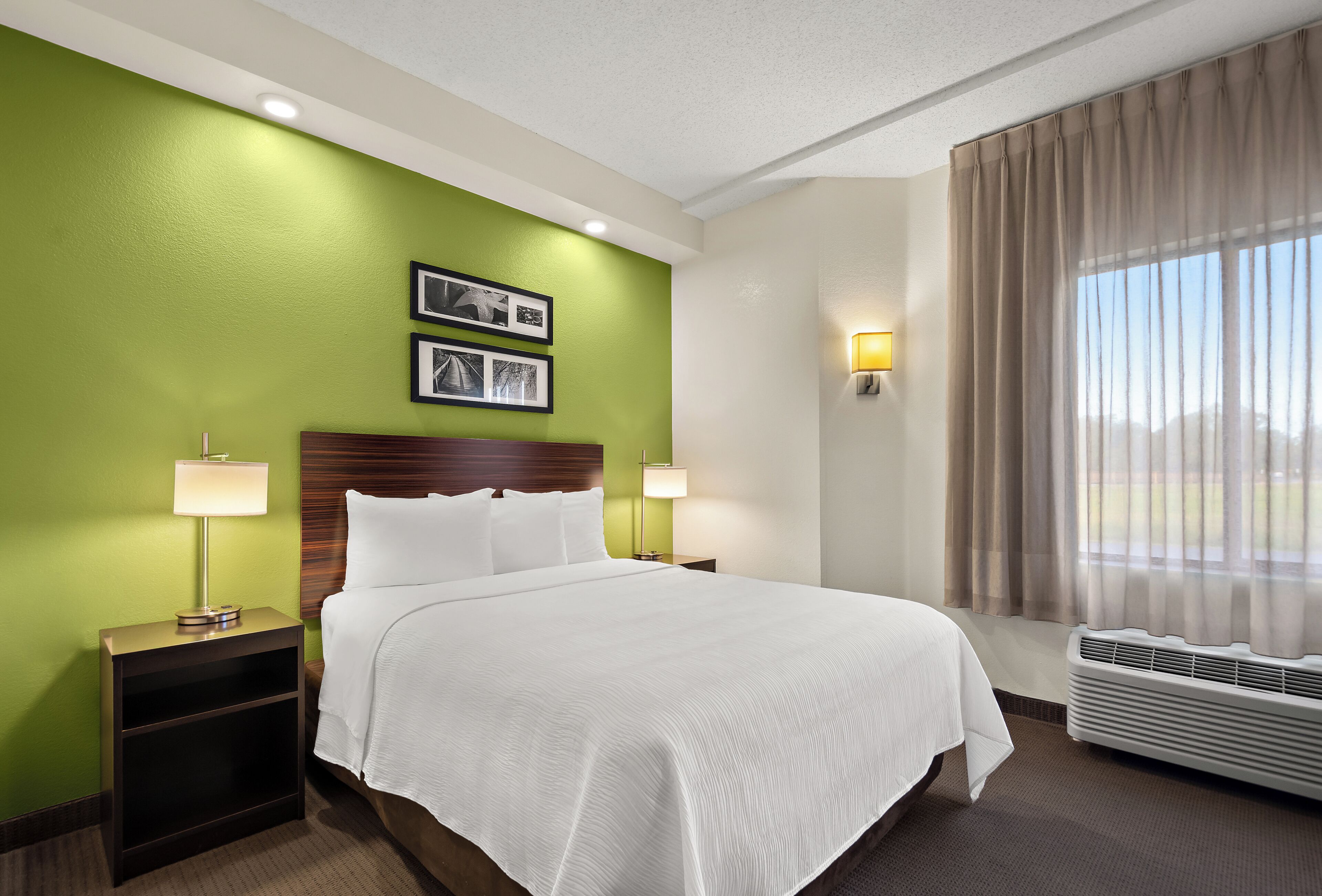 Habitación de hotel con una cama grande, paredes verdes, dos lámparas de noche, un cabecero y una ventana con cortinas.