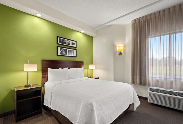 Habitación de hotel con una cama grande, paredes verdes, dos lámparas de noche, un cabecero y una ventana con cortinas.