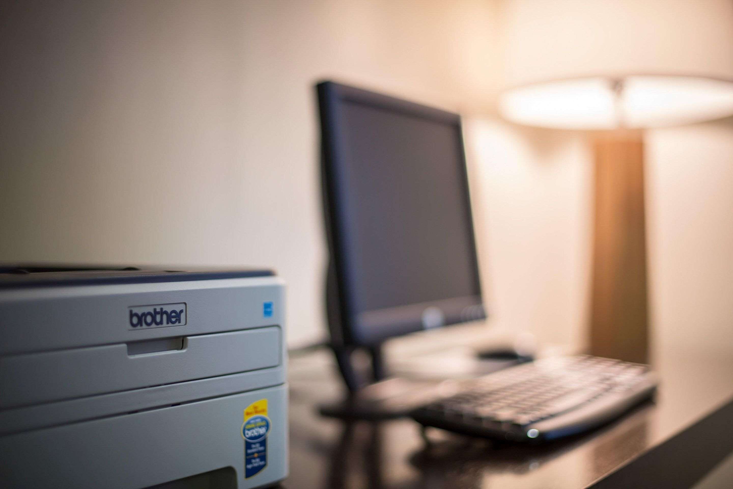 A Brother printer on a desk with a computer monitor and keyboard.