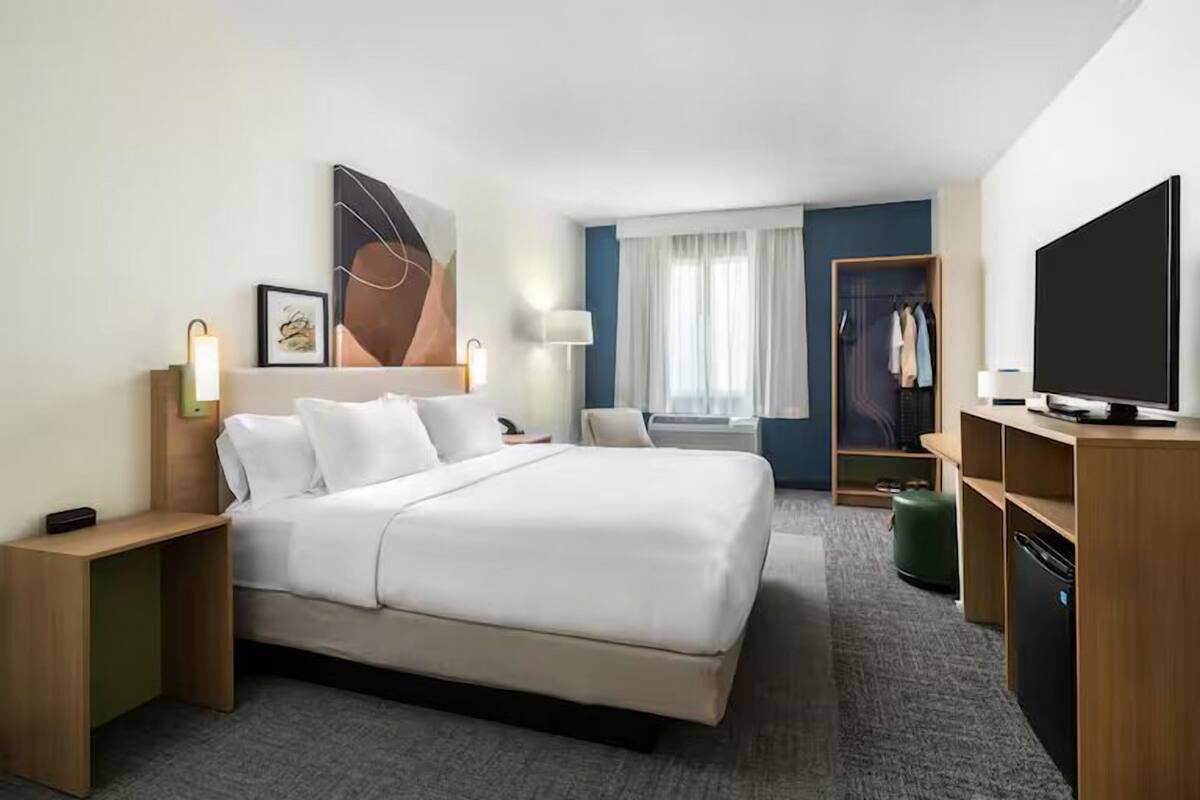 A hotel room with a bed, bedside tables, a TV, a wardrobe, and a window with curtains.