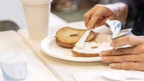 A person spreading cream cheese on a slice of bread on a plate. - Spark by Hilton Grand Rapids (Grand Rapids)
