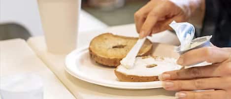 A person spreading cream cheese on a slice of bread on a plate.