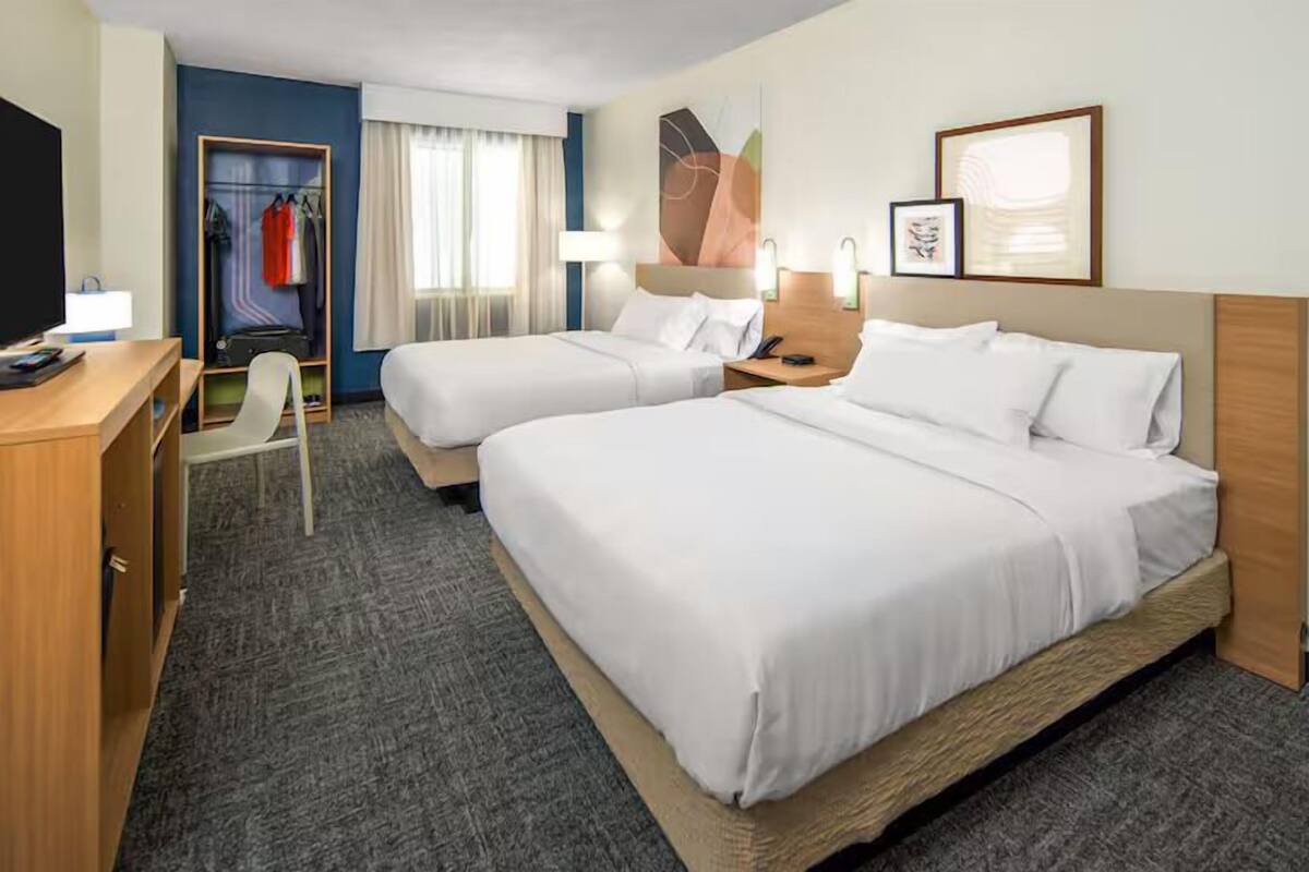 A hotel room with two beds, a desk, a chair, a wardrobe, and a television.