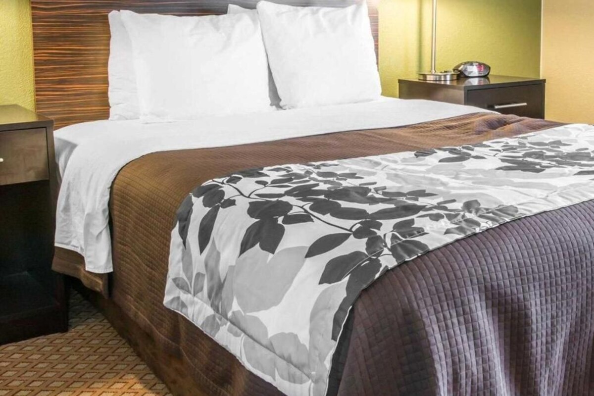 A hotel room with a bed, a nightstand, a lamp, and a wall with a textured pattern.