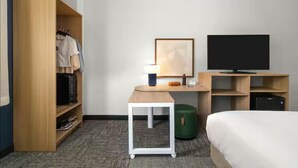 A hotel room with a bed, a desk with a lamp, a television, a wardrobe, and a trash bin. - Spark by Hilton Grand Rapids (Grand Rapids)