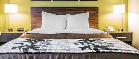 A hotel room with a bed, two bedside tables, a nightstand, a wooden headboard, and three framed pictures on the wall.