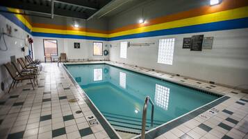 An indoor swimming pool with a checkered floor, a ladder, and a wall with safety signs.