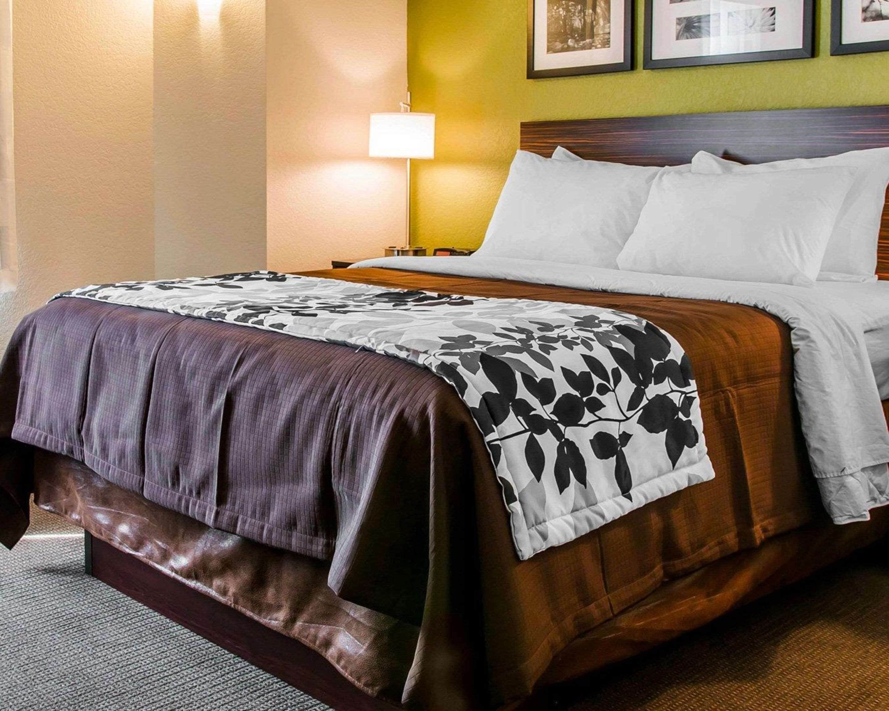 A neatly made bed with a brown headboard, a white pillow, and a floral-patterned blanket.