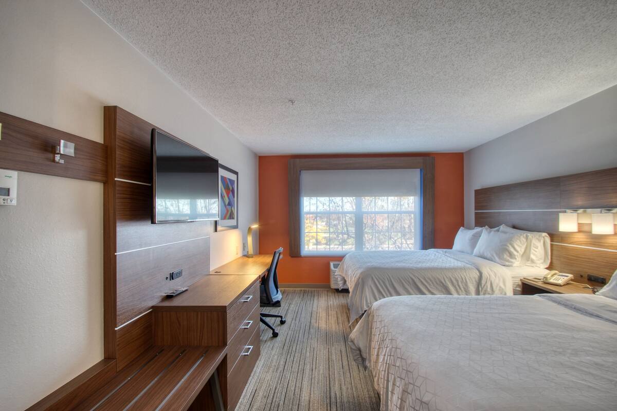 A hotel room with two beds, a desk, a TV, and a window with a view.