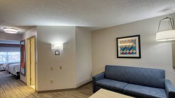 Habitación de hotel con sofá azul, una mesita, un cuadro en la pared y una puerta que da a otra habitación.