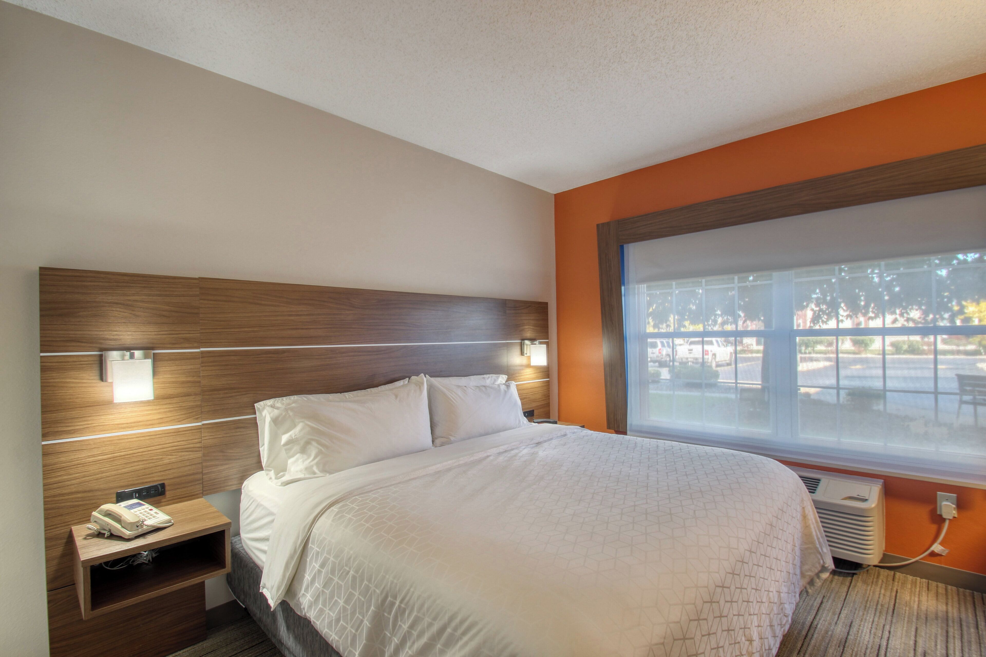 Una habitación de hotel con cama, mesita de noche y ventana con vistas al exterior.