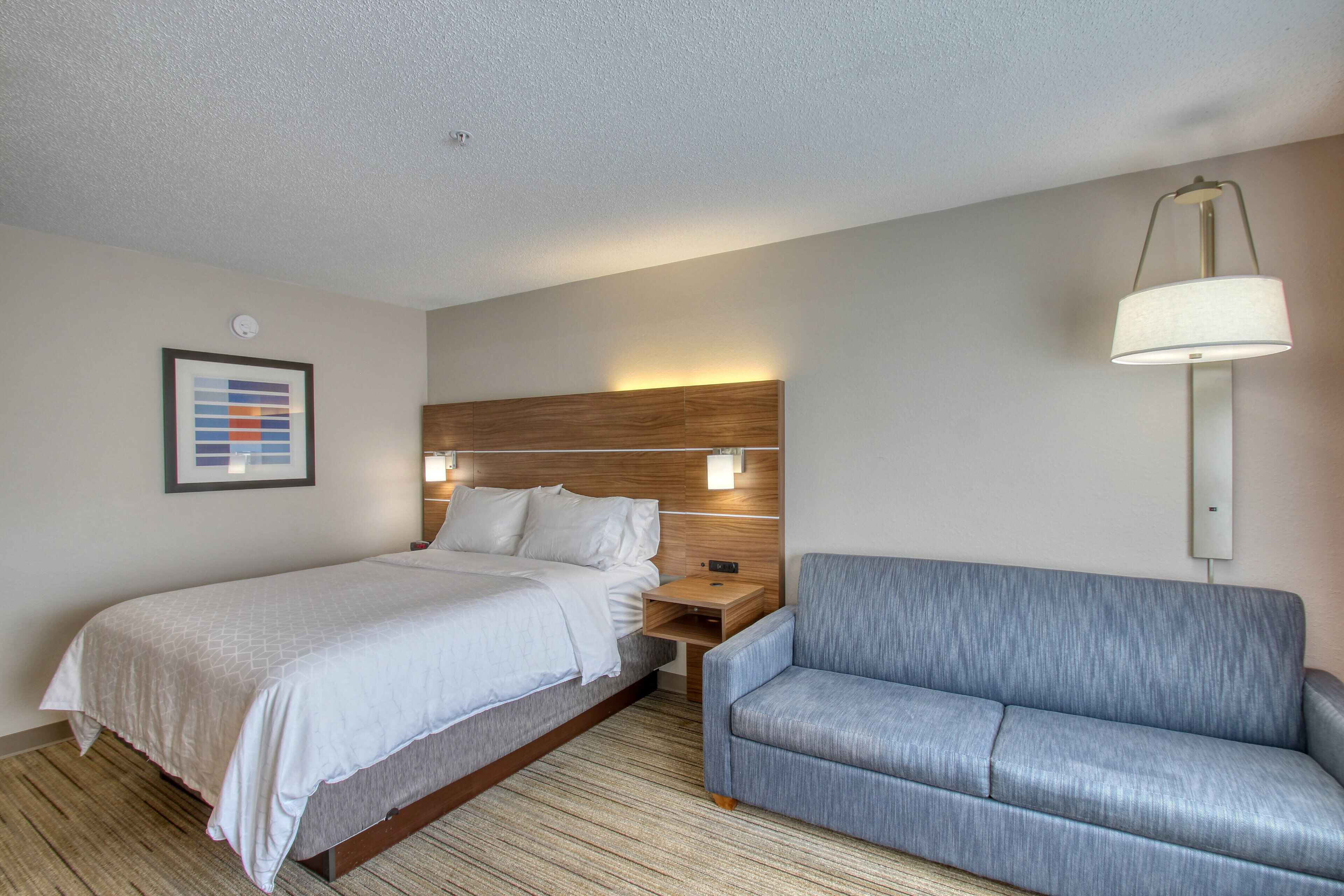 A hotel room with a bed, a nightstand, a lamp, and a sofa.