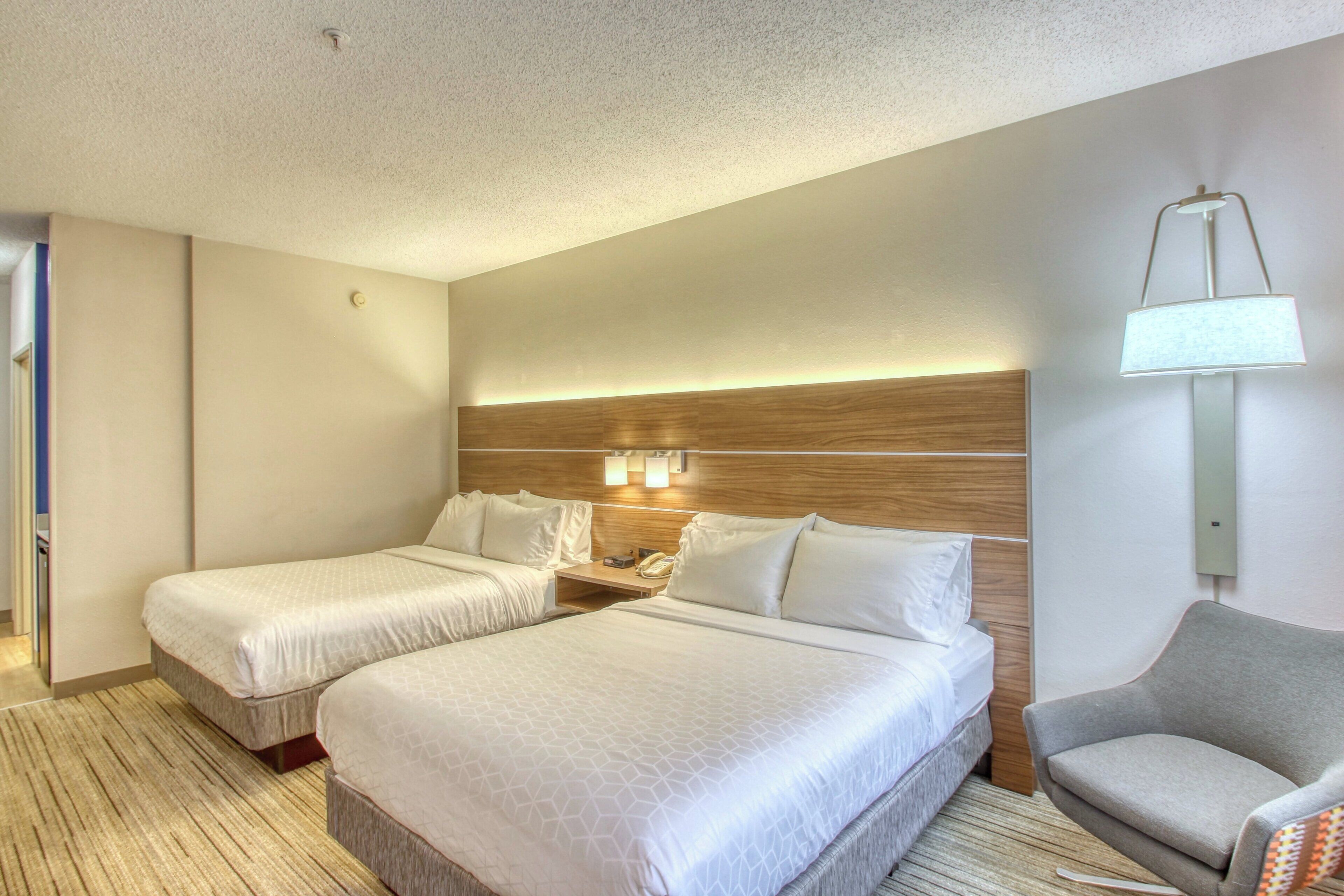 A hotel room with two beds, a nightstand, a lamp, and a chair.